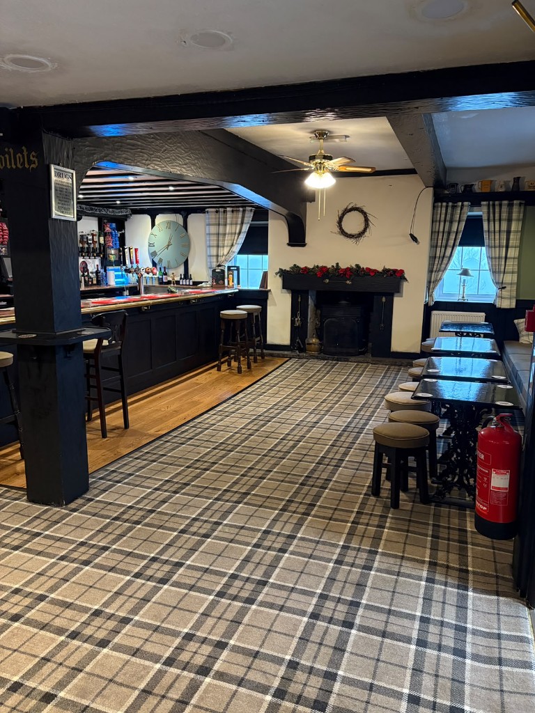 The bar room with a large clock, bar stools, wood-burning stove and tartan curtains