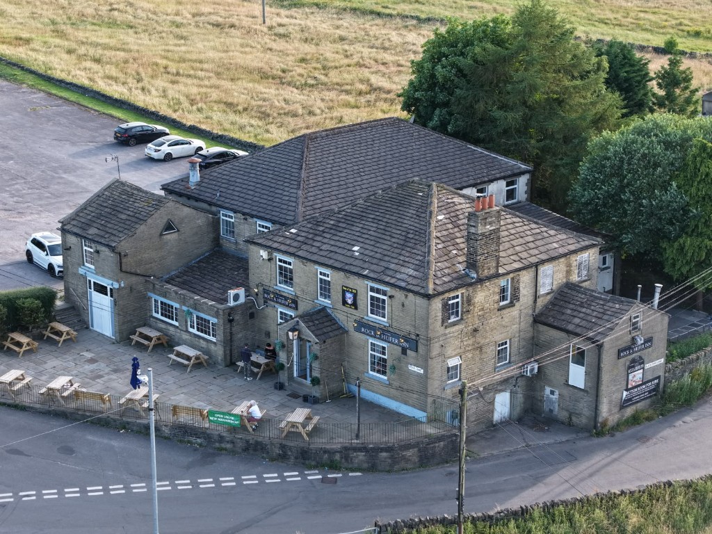 Aerial view of The Rock and Heifer, a stone pub on Rock Lane with picnic benches on the front terrace and a car park beside it