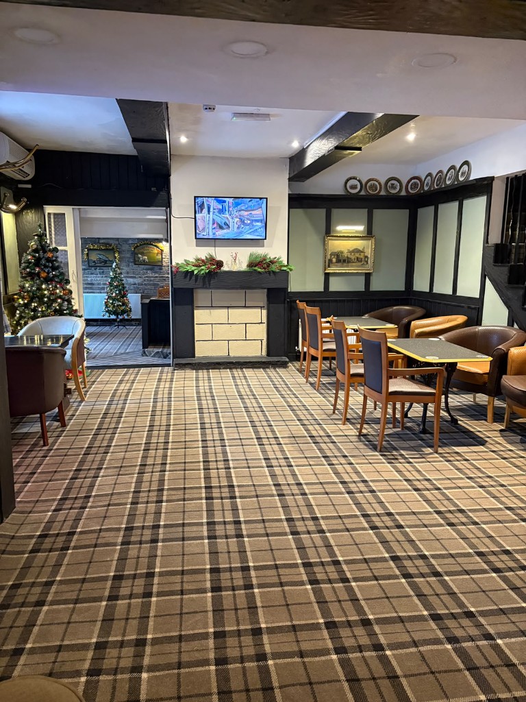 The lounge at The Rock and Heifer with tartan carpet, fireplace, wall-mounted TV and leather tub chairs