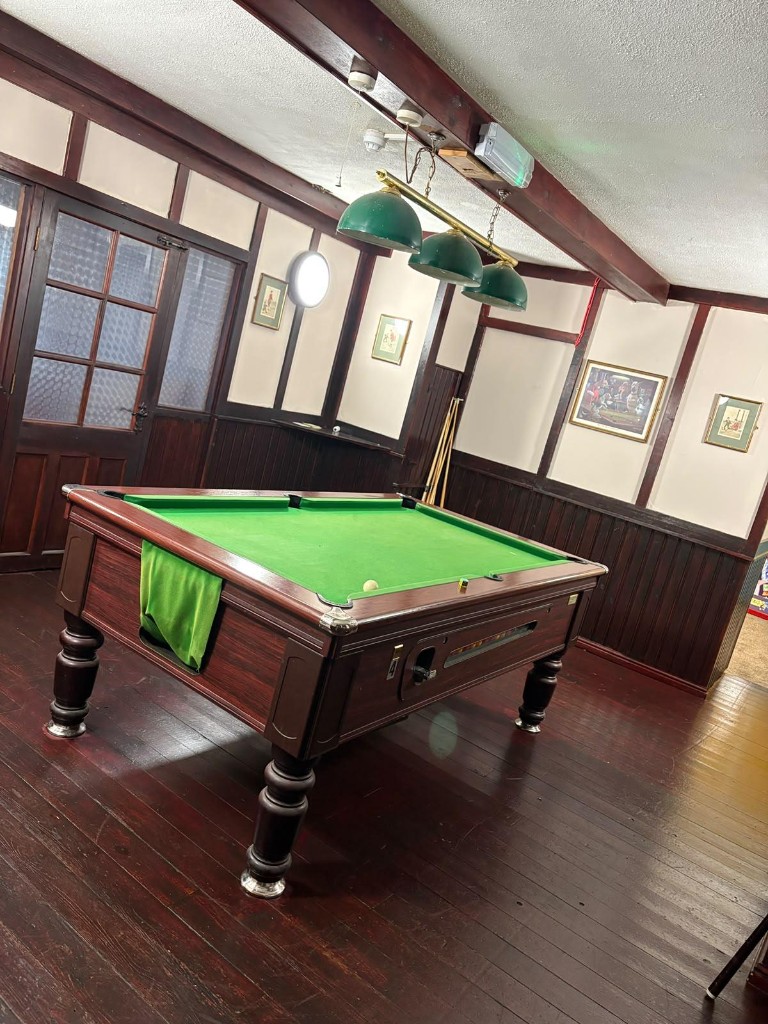 The pool room at The Rock and Heifer with a pool table under green pendant lamps and dark timber panelling