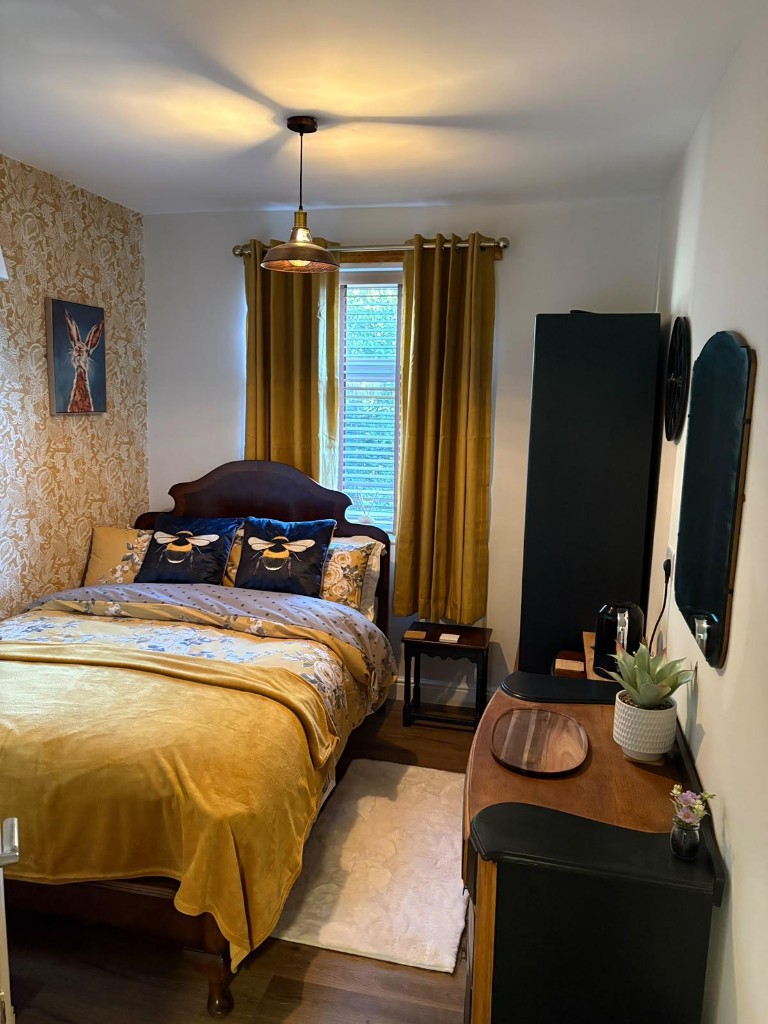 The Bee Room: a guest bedroom with mustard throw and curtains, bee-print cushions and floral wallpaper