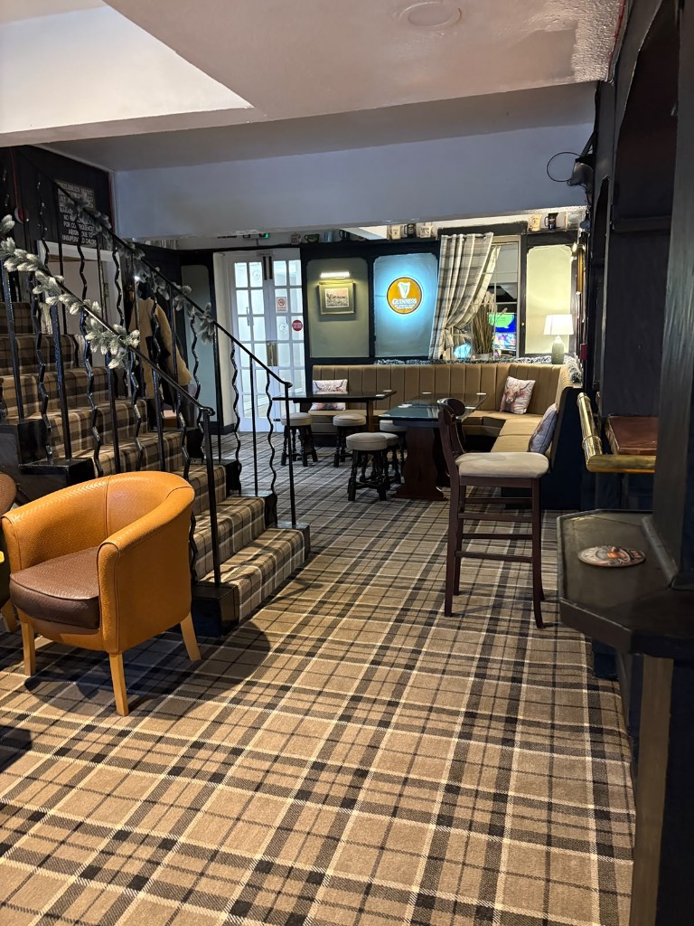 The snug at The Rock and Heifer with staircase, tartan carpet, banquette seating and Guinness sign